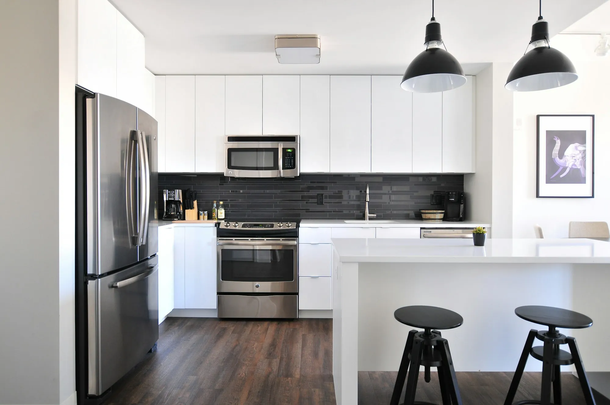 White kitchen with black pendant lights and stools at the island